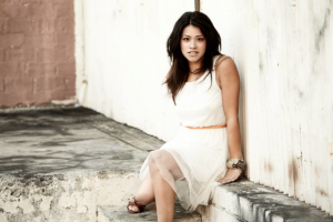 Gina Rodriguez posed for a photo, sitting on a ledge against a fence