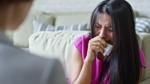 Woman with long black hair and pink blouse. She is crying with tissue in hand.