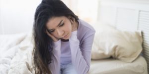 Sad Hispanic woman sitting at edge of bed