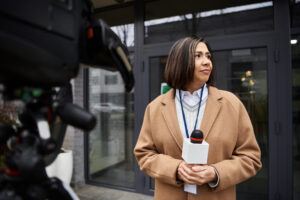 a multiracial woman journalist reports the news in front of a building